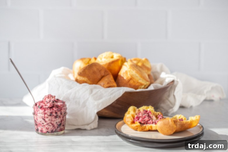 Close-up of a popover split open, revealing its airy interior, generously topped with blueberry basil butter