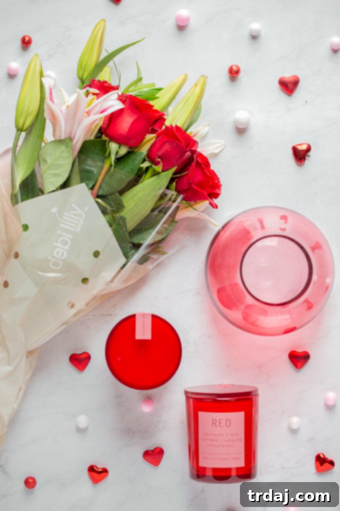 Exquisite debi lilly design™ fragrant rose bouquet in a stylish pink teardrop vase, alongside a beautifully scented red color meaning candle, all available exclusively at Jewel-Osco for Valentine's Day.