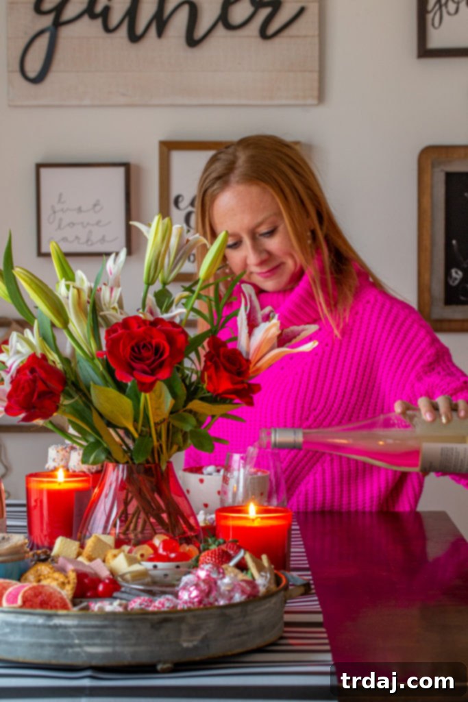 A charming lifestyle photo capturing the essence of a Valentine's Day tablescape, featuring a hand pouring wine into a glass amidst a vibrant spread of pink and red decor, including the dessert board and floral arrangements.