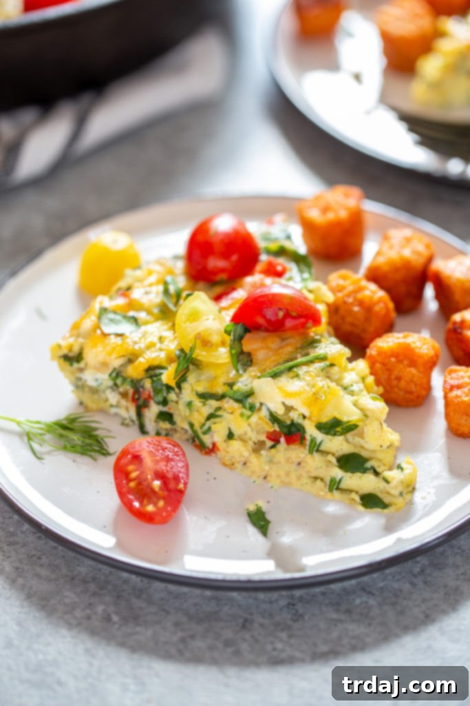 Close-up photograph of a Garden Herb Frittata slice served with sweet potato tots and cherry tomatoes