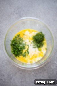 Eggs, cream, and herbs whisked together in a bowl