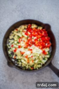 Close-up of softened red bell pepper, zucchini, and onion in a skillet