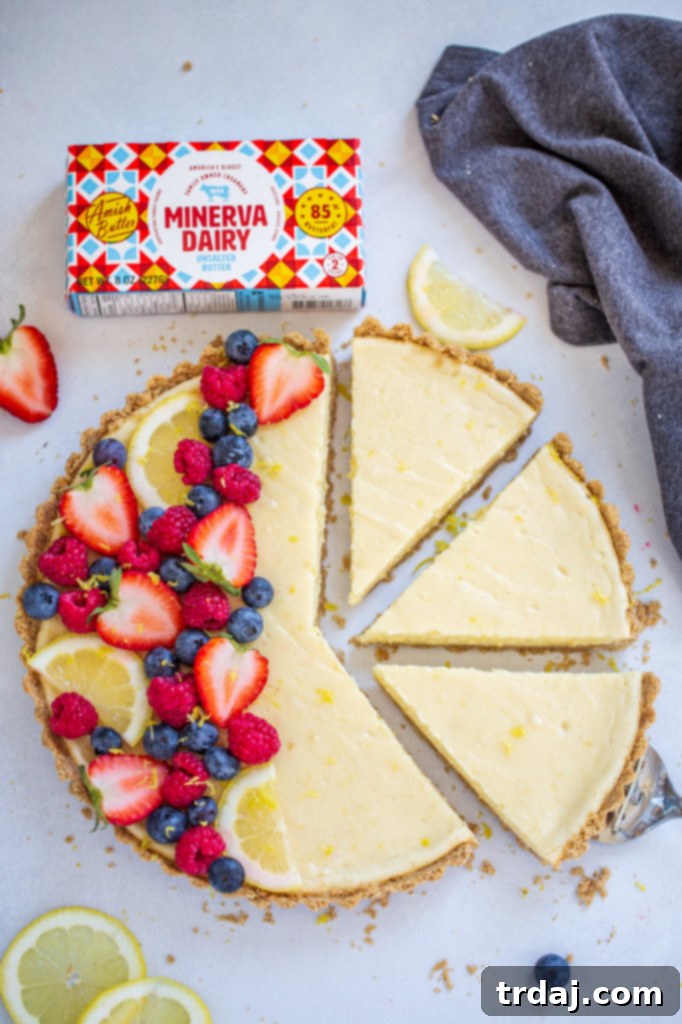 A slice of White Chocolate Lemon Cheesecake Tart on a plate, garnished with fresh berries and lemon zest