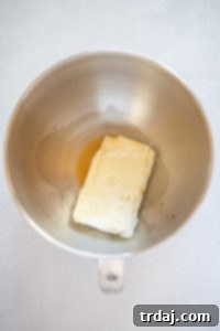 Cream cheese and vanilla extract mixing in a stand mixer bowl