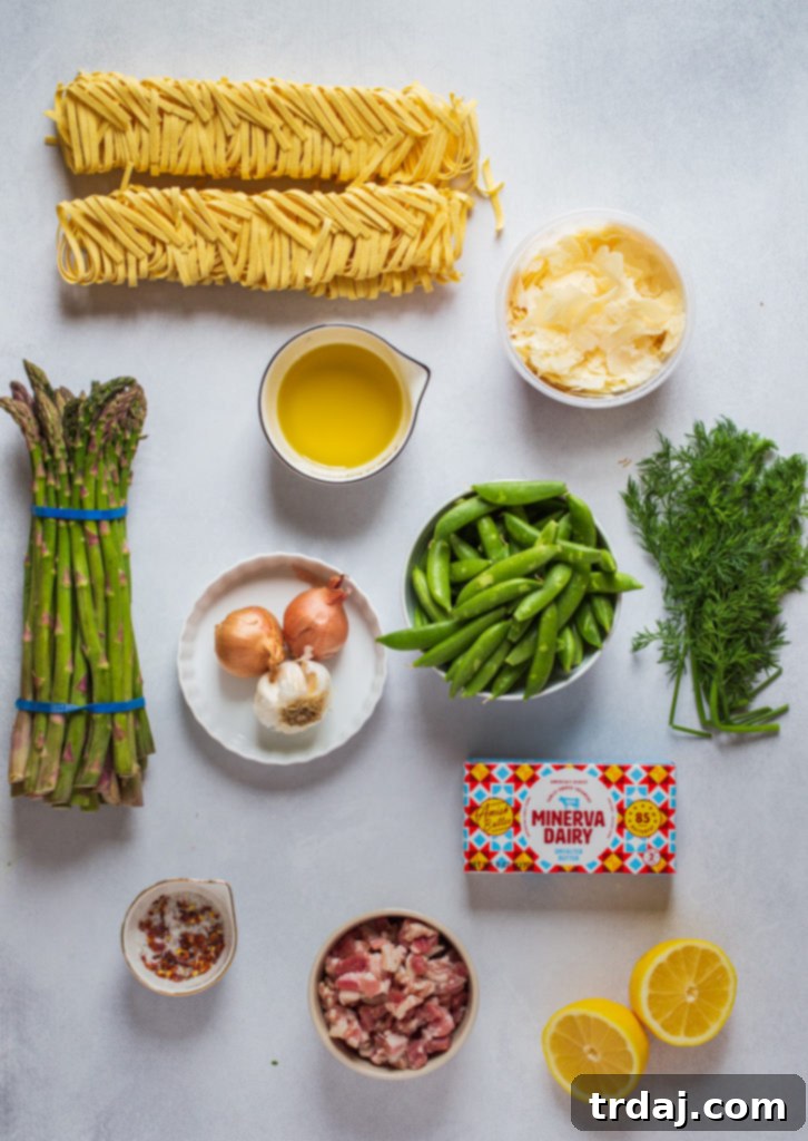 Overhead shot of all the fresh ingredients laid out on a wooden cutting board: pasta, asparagus, peas, lemon, garlic, shallots, and butter.