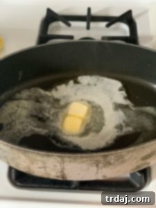 Pancetta sizzling in a skillet with melted butter.