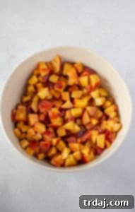 Bowl of chopped peaches generously covered in cornstarch, spices, brown sugar, and lemon, ready for the peach cobbler bars.