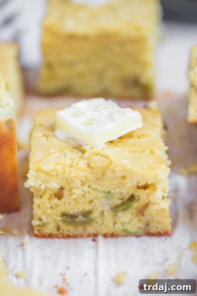 Single Serving of Roasted Green Chile Cornbread with Butter A single piece of golden-brown roasted green chile cornbread, with a pat of butter gently melting on its warm surface.