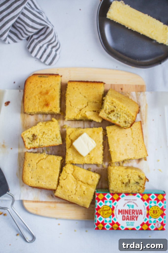 Homemade Roasted Green Chile Cornbread Squares A freshly baked pan of roasted green chile cornbread, cut into squares on a rustic wooden cutting board.