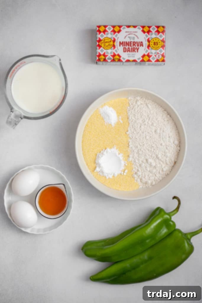 Ingredients for Roasted Green Chile Cornbread A selection of fresh ingredients laid out on a kitchen counter, including Anaheim peppers, flour, cornmeal, butter, eggs, honey, and buttermilk, ready for baking cornbread.