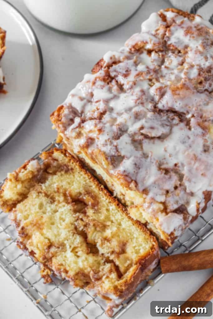 Overhead view of a whole apple fritter bread loaf with one slice cut, revealing the texture and glaze