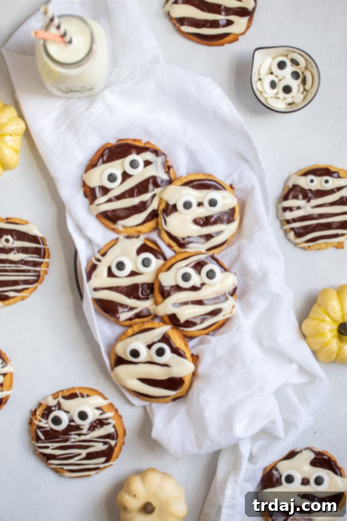 Peanut butter cookies decorated to look like mummies for Halloween, showcasing chocolate and vanilla drizzle with charming candy eyes.