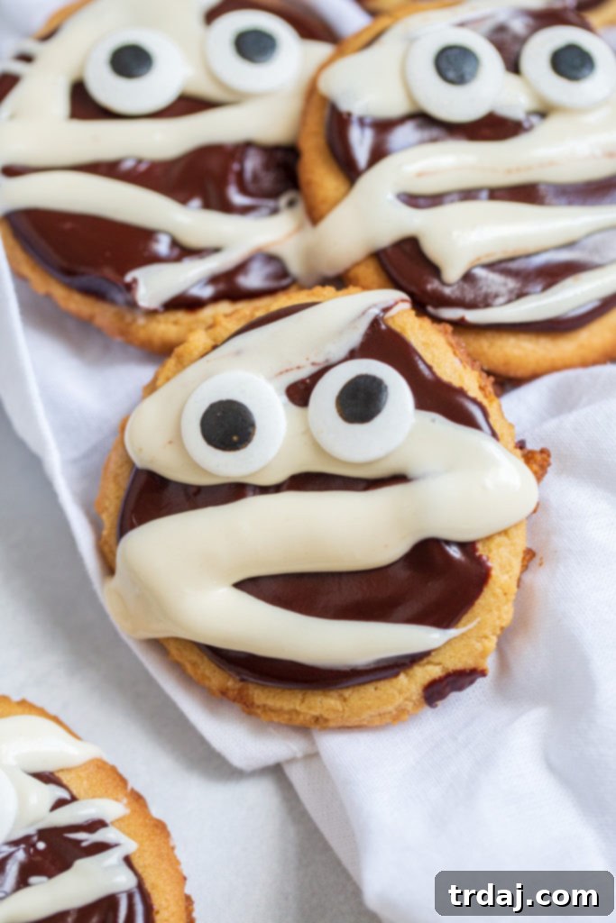 Close-up shot of chocolate peanut butter mummy cookies, highlighting the intricate vanilla glaze 'bandages' and playful candy eyes.