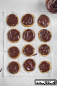 Peanut butter cookies meticulously covered with a smooth, rich layer of chocolate ganache, shown setting before the vanilla glaze is applied.