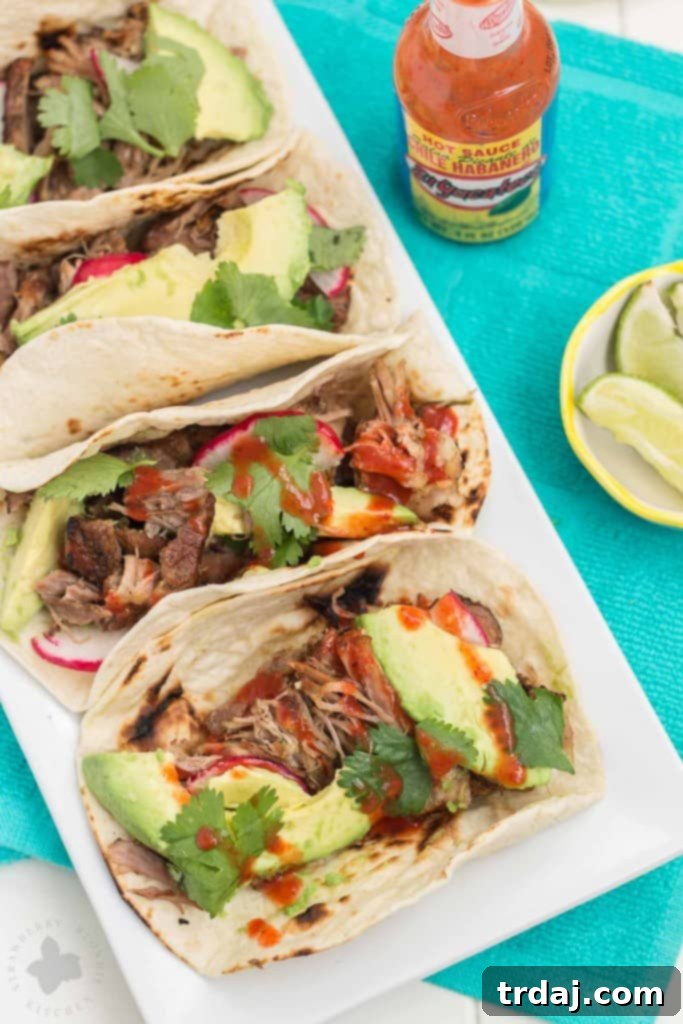 Plate of Slow Cooker Spicy Pork Carnitas on a charred tortilla, garnished with avocado, radish, cilantro, and a lime wedge.