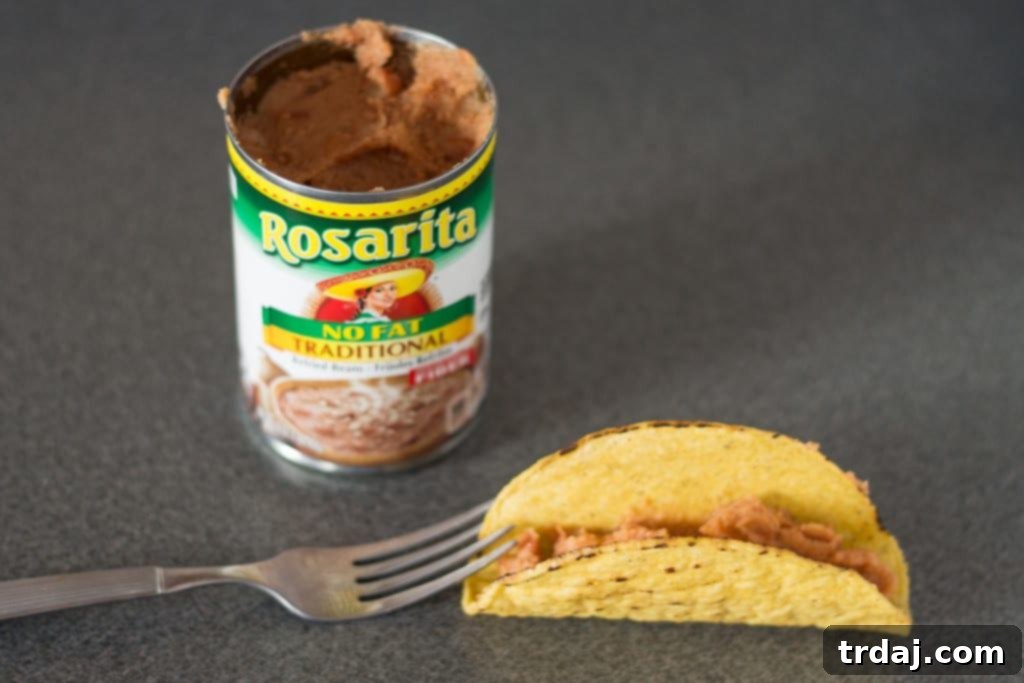 Kitchen hack: using a fork to keep taco shells upright while filling with refried beans.