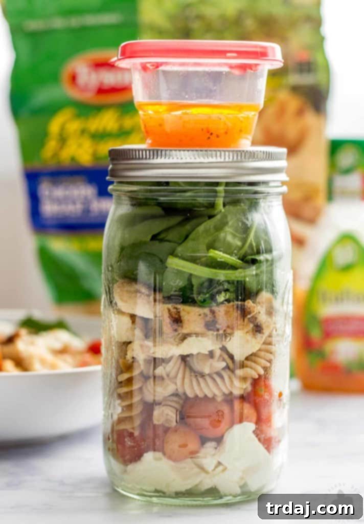 Ready-to-eat Layered Chicken Caprese Salad in a Jar, featuring fresh ingredients and a separate dressing container for ultimate freshness.