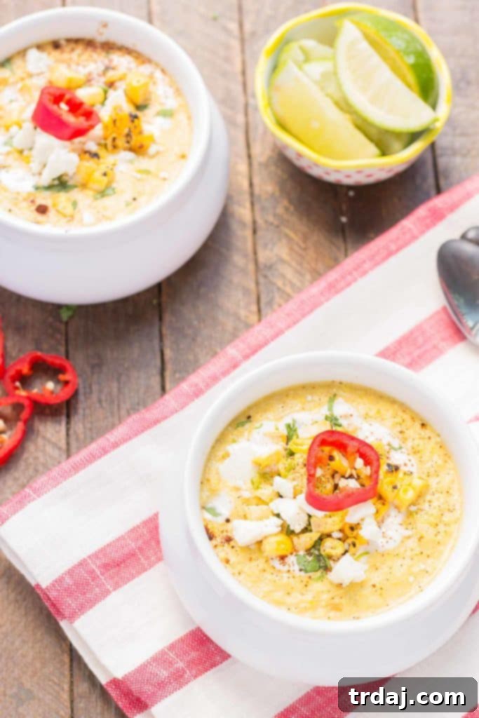 A bowl of creamy Mexican Street Corn Chowder garnished with fresh cilantro, cotija cheese, and a lime wedge. The rich yellow chowder is vibrant and inviting.