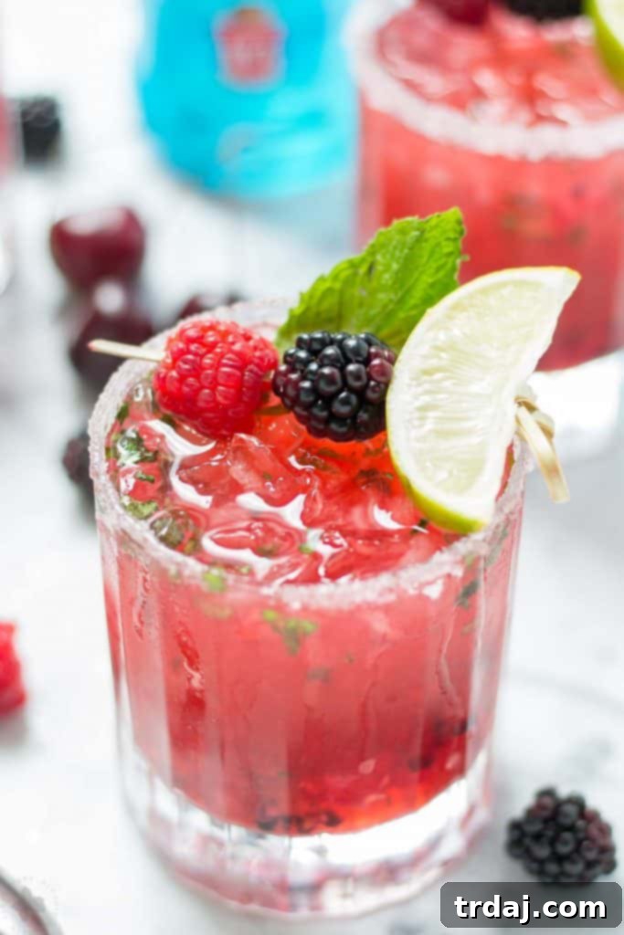 A collection of fresh ingredients for Triple Berry Mojitini, including mixed berries, mint, lime, and Smirnoff Red White & Berry vodka, ready for cocktail preparation.