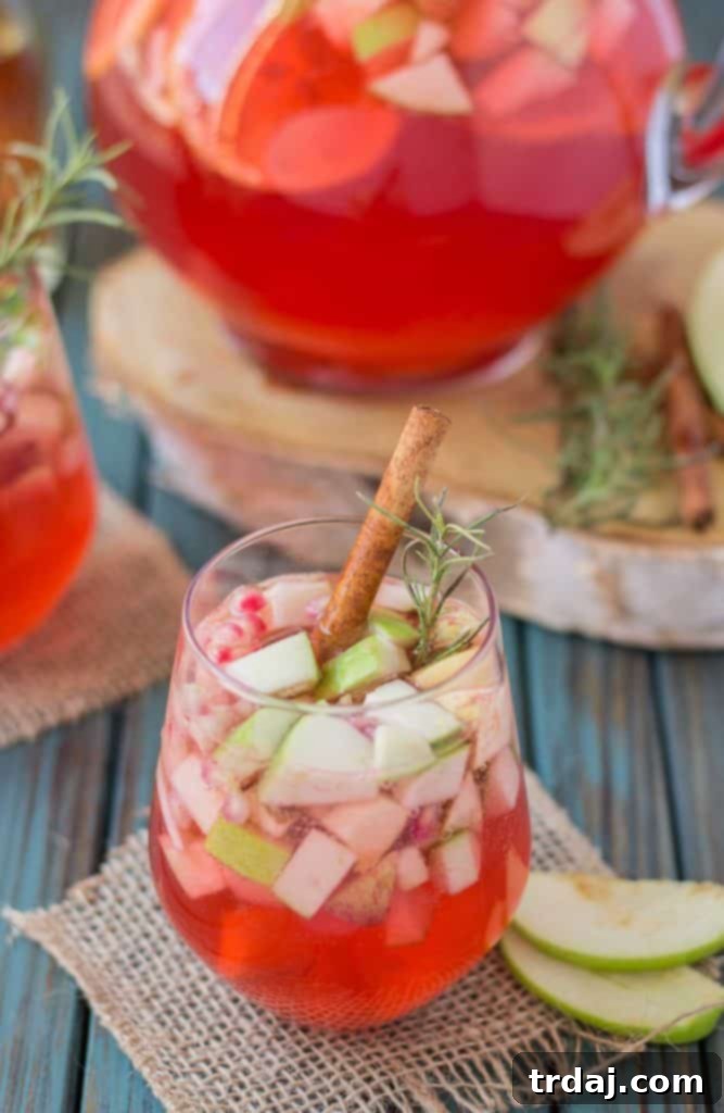 A second view of Cranberry Apple Rosemary Sangria in a pitcher, garnished with fresh apple slices, cranberries, and rosemary sprigs, ready for a fall gathering.