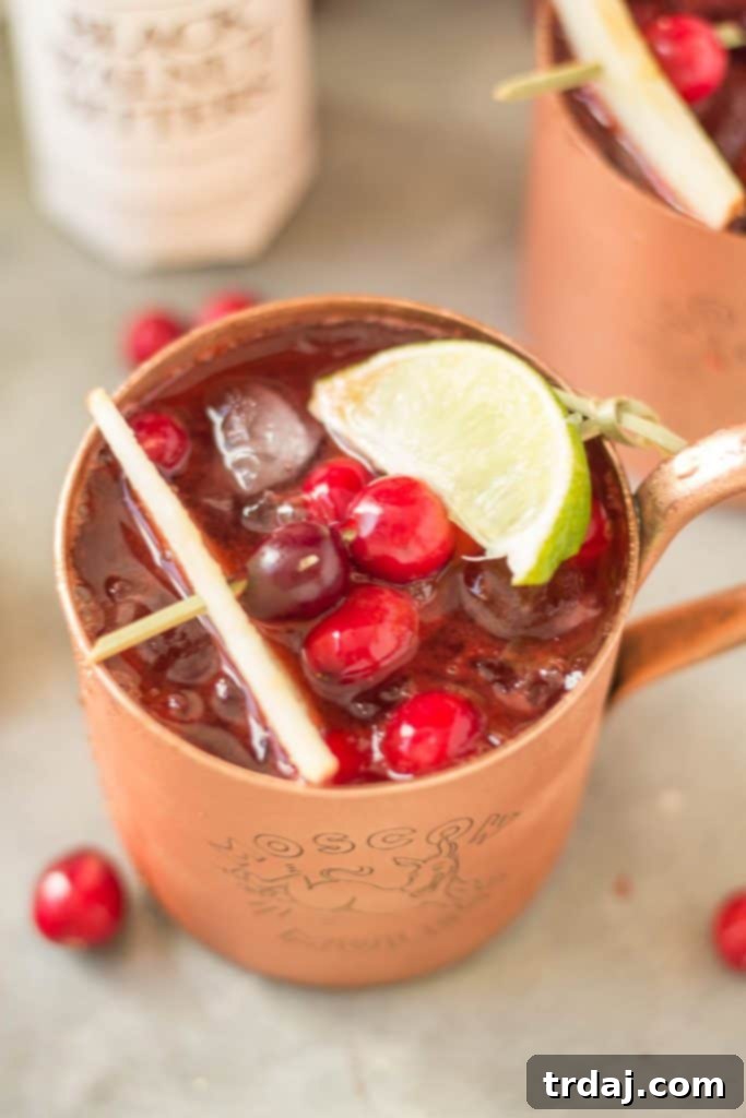Three copper mugs filled with Cranberry Apple Moscow Mules, garnished with fresh cranberries and lime, perfect for a fall gathering or autumn celebration.