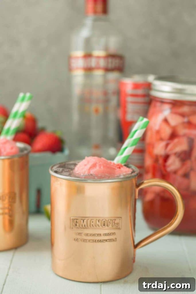 Overhead shot of two Strawberry Moscow Mule Floats in copper mugs, garnished with fresh strawberries and lime wedges, sitting on a wooden surface.