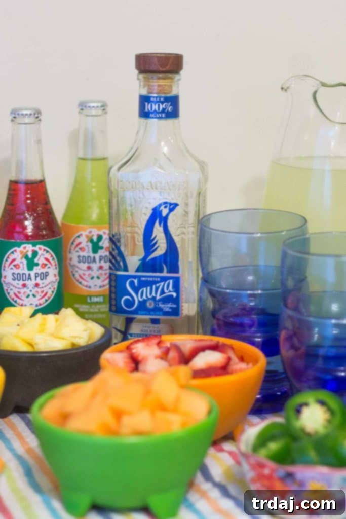 Sauza Tequila bottle prominently displayed next to a pitcher of classic margaritas and a variety of fresh fruits and herbs for a DIY margarita bar.