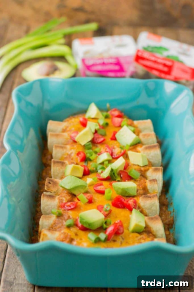 Uncooked Chipotle Chicken Enchiladas neatly arranged in a baking dish, topped with sauce and cheese.