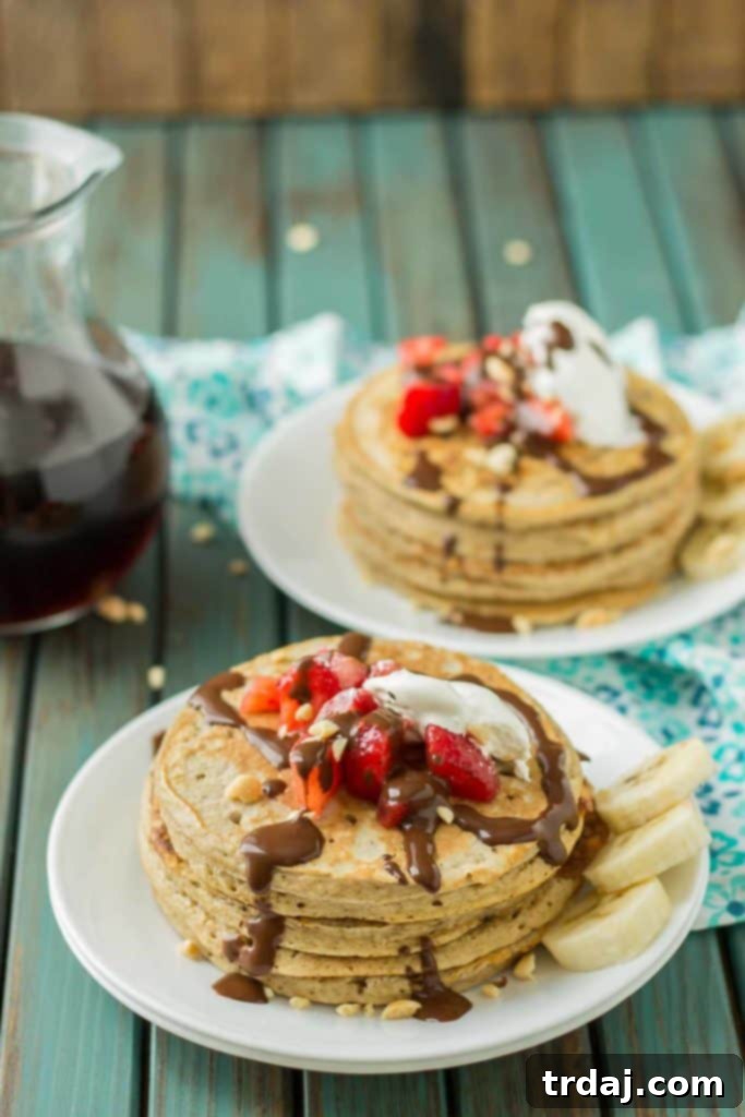 Close-up of fluffy Banana Split Pancakes, garnished with vibrant strawberries, whipped topping, and a drizzle of chocolate sauce.