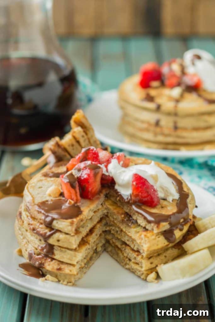 A close-up shot of a cooked banana split pancake, garnished with strawberries, whipped cream, chocolate syrup, and chopped peanuts.