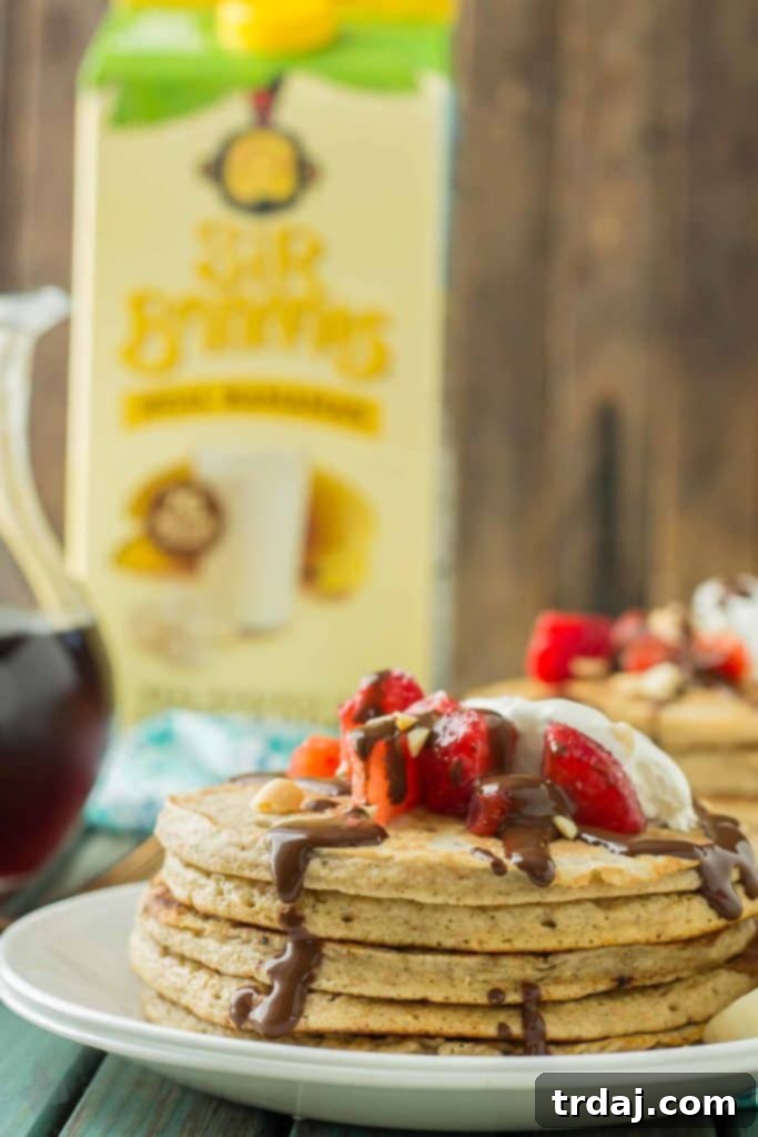 A vibrant breakfast scene featuring a bowl of banana split pancakes, fresh ingredients, and a glass of Sir Bananas® Bananamilk.