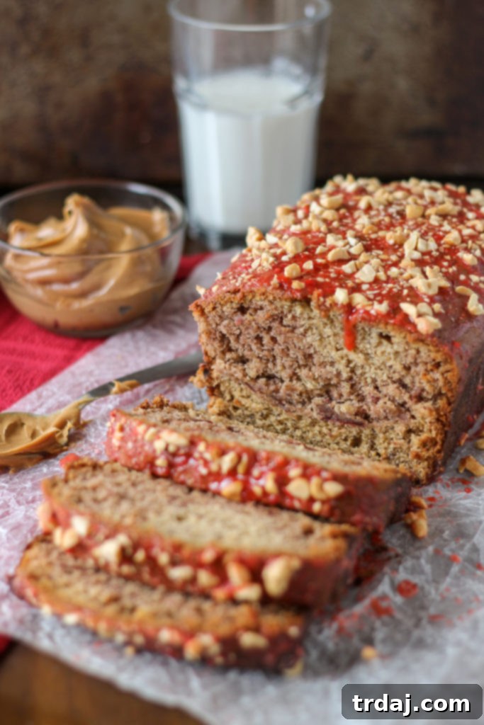 A beautifully sliced loaf of Peanut Butter and Jelly Banana Bread, showcasing a vibrant strawberry jelly swirl and crunchy peanut topping.