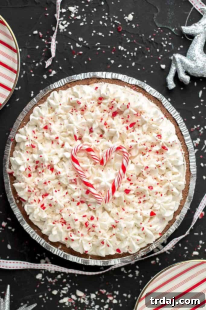 Festive No Bake Candy Cane Pie with Heart-Shaped Candy Cane Garnish An overhead shot of a whole No Bake Candy Cane Pie, beautifully garnished with candy canes forming a heart shape on top, surrounded by loose peppermint pieces, creating a stunning festive presentation.