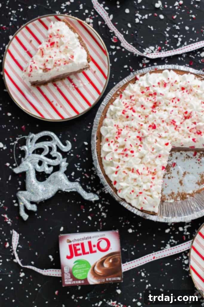 Ingredients and Slice of No Bake Candy Cane Pie A beautifully composed flat lay shot featuring a slice of No Bake Candy Cane Pie next to the whole pie, with a box of JELL-O chocolate pudding visible in the background, highlighting key ingredients.