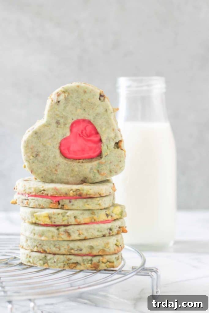 Grinch Sandwich Cookies: Festive green pistachio shortbread with a red heart cutout, evoking the spirit of Dr. Seuss's How the Grinch Stole Christmas. Delicious holiday cookie recipe.