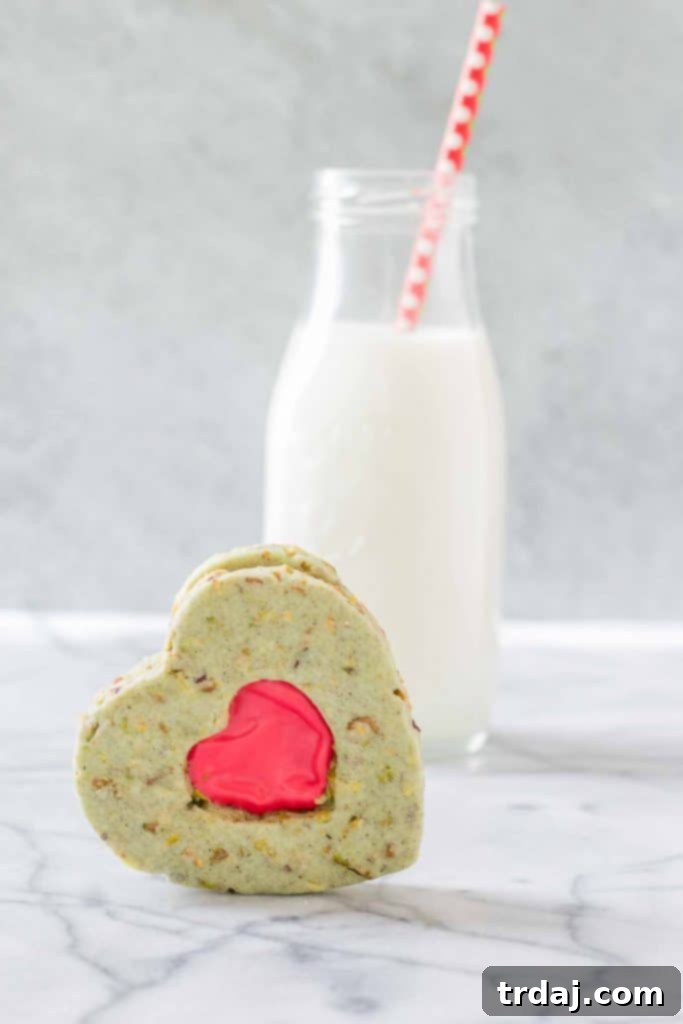 Platter of freshly baked Grinch Sandwich Cookies, highlighting their uniform heart shapes, rich green color from pistachios, and smooth red filling. Ideal for holiday dessert tables.