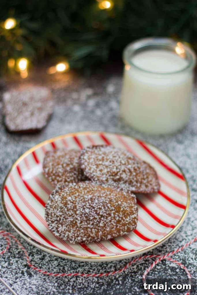 A stack of Gingerbread Madeleines on a rustic wooden board, dusted lightly with powdered sugar, creating a festive and inviting scene. The warmth of the gingerbread spices seems to emanate from the image.