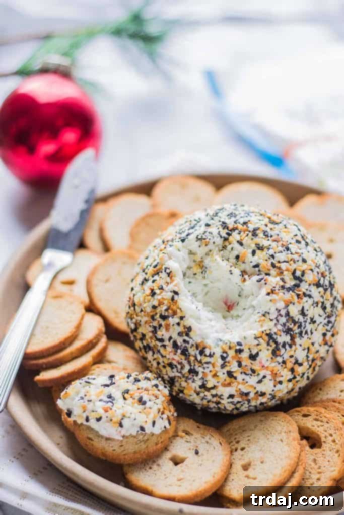Hands carefully rolling the prepared cheese ball mixture into a plate of everything bagel seasoning, ensuring full and even coverage.