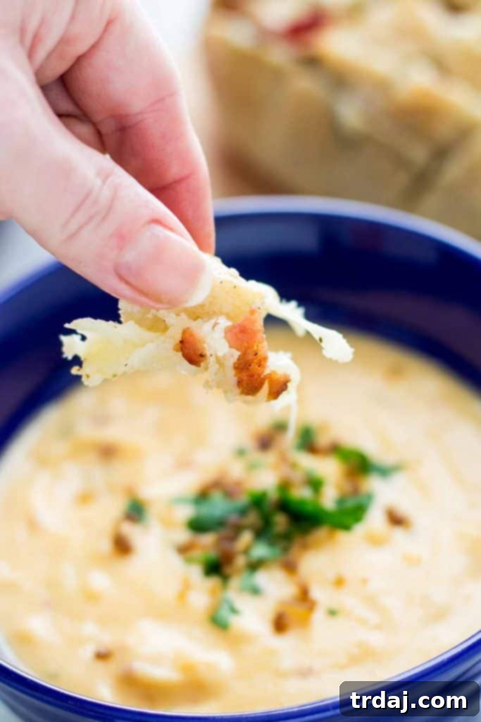 Close-up of a hand tearing a piece of Cheddar Bacon Ranch Pull Apart Bread, revealing gooey cheese and bacon, ready to be dipped into soup.