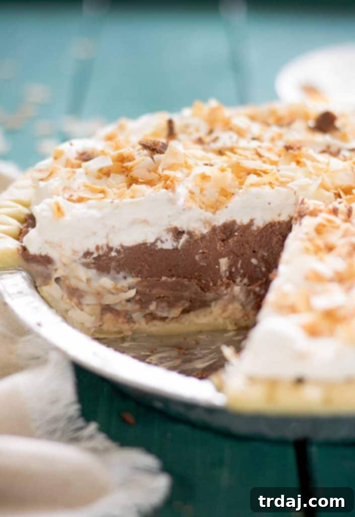 A delicious slice of Chocolate Coconut Cream Pie, showcasing its beautiful layers of chocolate, coconut, and whipped cream on a plate. A generous, perfectly cut slice of Chocolate Coconut Cream Pie served on a white plate, clearly showing the distinct chocolate, coconut, and whipped cream layers, ready to be enjoyed.