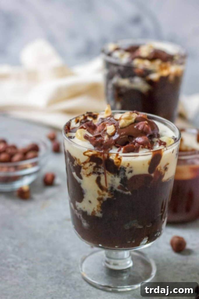 A large serving of Hazelnut Pudding Cake in a bowl, topped generously with ice cream, chopped hazelnuts, and chocolate syrup